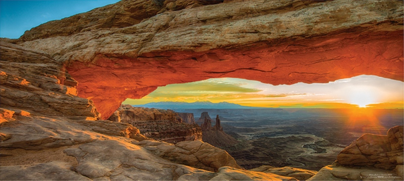 Glowing underside of Mesa Arch framing sunlit desert spires and distant ridges near Moab, Utah