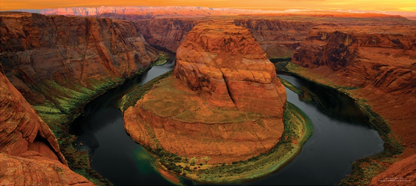 Colorado River curving around the sandstone cliffs at Horseshoe Bend beneath an orange sky